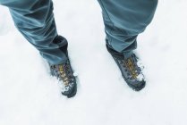 Сверху неузнаваемый турист в треккинговых сапогах зимой стоит на заснеженной земле — стоковое фото