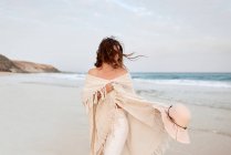 Женщина-путешественница в солнцезащитных очках и шляпе, идущая вдоль берега моря и отводящая взгляд — стоковое фото