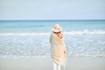 Back view female traveler in hat walking along seashore and looking away — Stock Photo