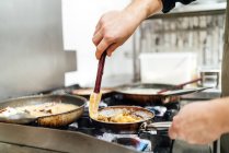 Crop unrecognizable chef salting and seasoning pans of appetizing dishes preparing on stove in restaurant kitchen — Stock Photo