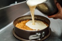 Cropped unrecognizable cook pouring cream on cake tin while preparing delicious cheesecake dessert in cafe — Stock Photo