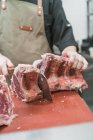 Cortar açougueiro macho irreconhecível em avental cortando carne com faca afiada durante o trabalho na cozinha — Fotografia de Stock