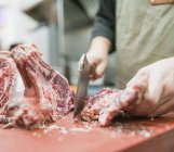 Cultiver boucher mâle méconnaissable dans tablier hacher la viande avec un couteau tranchant pendant le travail dans la cuisine — Photo de stock