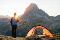 Повернення до нерозпізнаного мандрівника, що стоїть на пагорбі біля намету з видом на мальовничий гірський пасмо Піренеїв вранці. — стокове фото