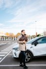 Busy male entrepreneur with attache case standing on parking lot near car and speaking on mobile phone while discussing project and looking away — Stock Photo
