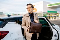 Confident male entrepreneur in coat and with attache case getting out of modern automobile and looking away — Stock Photo