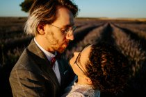 Visão lateral de alto ângulo de casal recém-casado romântico em pé face a face no campo espaçoso contra o céu púrpura pôr do sol — Fotografia de Stock