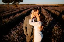 High angle side view of romantic newlywed couple standing face to face kissing on spacious field against purple sunset sky — Stock Photo