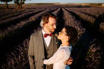 Hochwinkelseitenansicht des romantischen Brautpaares, das Gesicht zu Gesicht auf einem weitläufigen Feld vor lila Sonnenuntergangshimmel steht — Stockfoto
