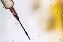 Крупный план иглы шприца, наполненного вакциной от вируса, введенного в клетку на размытом фоне — стоковое фото