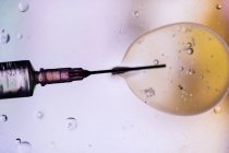 Nahaufnahme einer mit Impfstoff gefüllten Spritze aus Virus, das in Zelle injiziert wurde, auf verschwommenem Hintergrund — Stockfoto