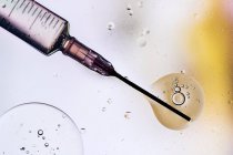 Крупним планом голка шприца, наповнена вакциною від вірусу, введеного в клітину на розмитому фоні — стокове фото