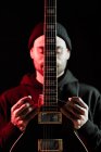 Tranquille musicien rock masculin debout avec guitare électrique sur fond noir en studio avec lumière rouge — Photo de stock