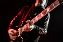 Низький кут рок-гітариста, який грає на електрогітарі під час виступу в темній студії з червоним світлом — стокове фото