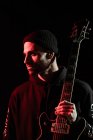 Tranquille musicien rock masculin debout avec guitare électrique sur fond noir en studio avec lumière rouge — Photo de stock