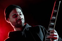 Niedriger Winkel des Rockgitarristen, der E-Gitarre spielt, während er im dunklen Studio mit rotem Licht auftritt — Stockfoto