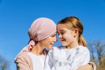 Glückliche krebskranke Mutter mit rosa Kopftuch umarmt kleine Tochter im grünen Park und schaut sich an — Stockfoto