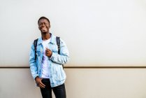 Junger fröhlicher schwarzer Mann in Jeansjacke schaut bei Tageslicht mit zahmem Lächeln weg — Stockfoto
