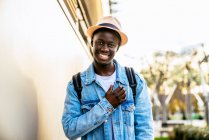 Jovem homem negro alegre em casaco de ganga olhando em frente com um sorriso de dente à luz do dia. — Fotografia de Stock