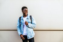 Молодой веселый черный мужчина в джинсовой куртке смотрит в сторону с зубастой улыбкой при дневном свете — стоковое фото