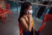 Ritratto di giovane donna afro latina attraente che indossa una maschera facciale e parla su smartphone in un centro commerciale, Colombia — Foto stock