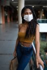 Portrait d'une jolie jeune femme afro latine portant un masque et tenant des sacs à provisions dans un centre commercial, Colombie — Photo de stock