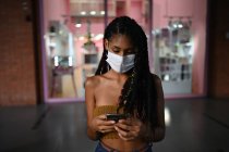 Портрет привлекательной молодой афро-латиноамериканской женщины в маске и со смартфоном в торговом центре, Колумбия — стоковое фото