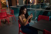 Retrato de atraente jovem afro-latina usando um smartphone em um shopping comercial, Colômbia — Fotografia de Stock