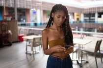 Retrato de luz de fundo de atraente jovem afro mulher latina usando um smartphone em um shopping comercial, Colômbia — Fotografia de Stock
