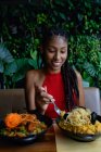 Портрет привабливої жінки африканського латину з дредами в червоному крохті, що харчується в азіатському ресторані (Колумбія). — стокове фото