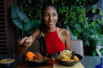 Портрет привабливої жінки африканського латину з дредами в червоному крохті, що харчується в азіатському ресторані (Колумбія). — стокове фото
