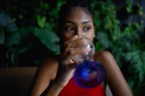 Jovem mulher latina afro atraente com dreadlocks em um top vermelho de crochê bebe água no restaurante, Colômbia — Fotografia de Stock