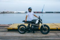 Selbstbewusster junger bärtiger Mann in weißem T-Shirt und Jeans beim Motorradfahren am Meer — Stockfoto