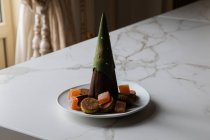 Шоколадний десерт у формі ялинки на тарілці з різними печивом та мармеладом, поданий на мармуровому столі у стильному ресторані — стокове фото