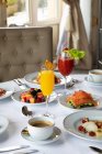 Vari piatti colorati e succhi di frutta serviti sulla tavola rotonda durante la colazione nell'elegante ristorante dell'hotel al mattino soleggiato — Foto stock