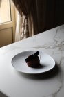 Высокий угол вкусного шоколадного глазурованного торта украшен съедобным украшением подается на белой тарелке и помещается на мраморный стол — стоковое фото