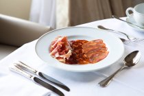 Von oben verschiedene Marmeladen- und Chorizo-Scheiben auf weißem Teller serviert und auf runden Tisch mit Kaffeebecher und Besteck im eleganten Restaurant platziert — Stockfoto