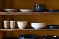 Set di stoviglie varie composto da piatti tazze e ciotole poste su ripiani in legno — Foto stock