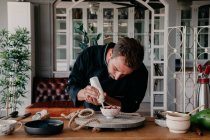 Concentrado jovem chef masculino em uniforme usando seringa creme ao decorar tigela com bagas frescas em pé à mesa em restaurante elegante — Fotografia de Stock
