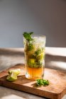 Refreshing cold alcoholic mojito with ice mint leaves and cut lime on wooden board — Stock Photo