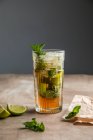 Mojito alcoolique froid rafraîchissant avec feuilles de menthe glacée et citron vert coupé sur une planche de bois — Photo de stock