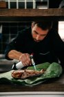 Концентрированный шеф-повар-мужчина готовит жареную рыбу с газовой горелкой во время работы в ресторане морепродуктов — стоковое фото