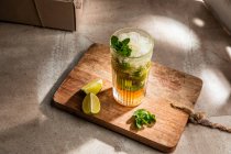Von oben erfrischend kalter alkoholischer Mojito mit Minzblättern und geschnittener Limette auf Holzbrett — Stockfoto
