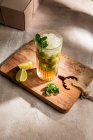 Dall'alto di rinfrescante mojito alcolico freddo con foglie di menta ghiaccio e calce tagliata su tavola di legno — Foto stock