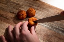 From above of crop anonymous cook cutting crispy deep fried cheese ball on wooden cutting board — Stock Photo