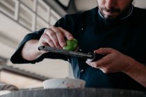 Cropped unrecognizable concentrated man rubbing zest of lime fruit during cooking process at counter of stylish kitchen — Stock Photo
