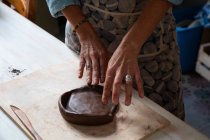 Зверху урожаю анонімний чоловічий майстер прокатки глини шматок при створенні тарілки в майстерні — стокове фото