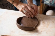 From above of crop anonymous male artisan rolling clay piece while creating plate in workshop — Stock Photo