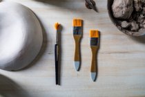 Set von Töpfern und Pinseln auf Holztisch mit Tonschale und Keramiktopf in der Werkstatt — Stockfoto