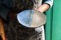 Урожай неузнаваемый ремесленник в фартуке демонстрирует творческую керамическую плиту в мастерской — стоковое фото